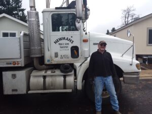 A man standing in front of a semi truck carrying 8 homes.