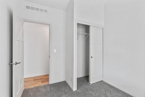 An empty room with white closets and hardwood floors.